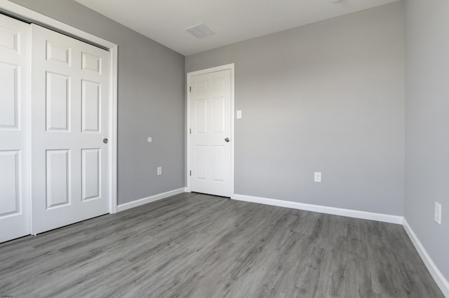 unfurnished bedroom featuring wood finished floors, baseboards, and a closet