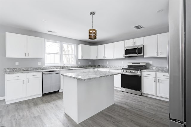 kitchen with appliances with stainless steel finishes, white cabinetry, a kitchen island, light stone countertops, and light wood-style flooring