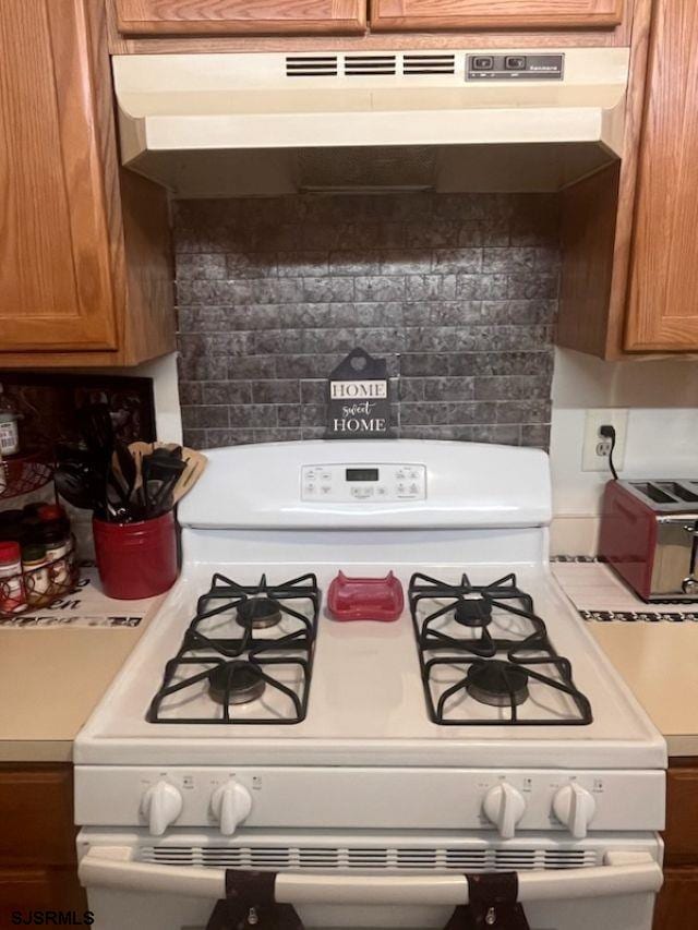 27 Sussex Pl Unit 27, Galloway Township, NJ 08205 - kitchen view of white range with gas stovetop, under cabinet range hood, light countertops, backsplash, and brown cabinetry