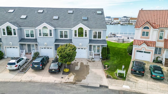 townhome / multi-family property featuring a shingled roof, stucco siding, driveway, a water view, and a front yard