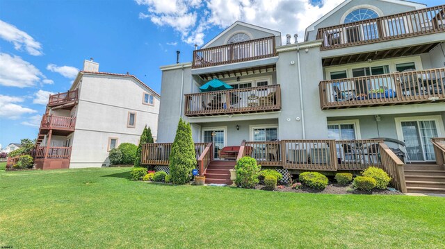 back of property with a balcony, a yard, and stucco siding