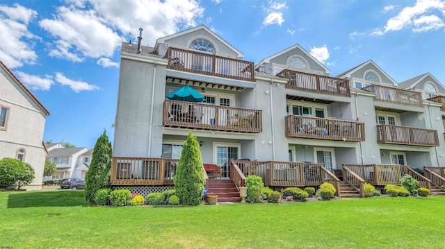 back of property featuring a balcony, a lawn, and stucco siding