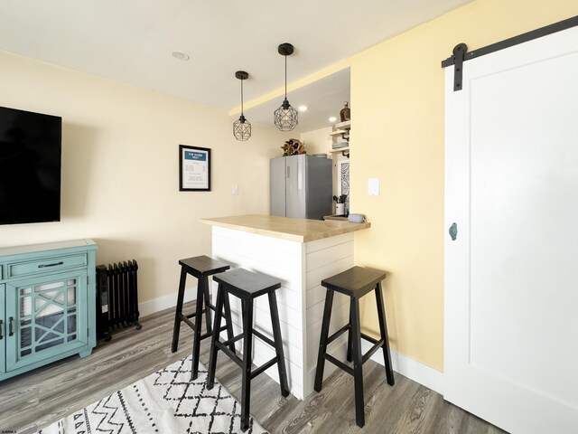 kitchen featuring freestanding refrigerator, wood finished floors, a barn door, a breakfast bar, and baseboards