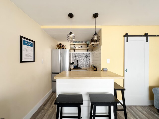 kitchen featuring wood finished floors, a barn door, freestanding refrigerator, a kitchen bar, and baseboards