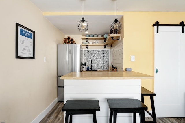 kitchen featuring freestanding refrigerator, dark wood finished floors, a barn door, baseboards, and a kitchen breakfast bar