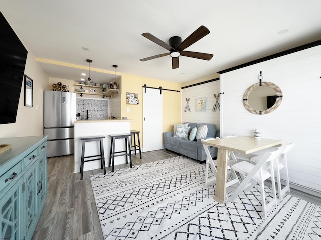 living area with a barn door, ceiling fan, and dark wood finished floors