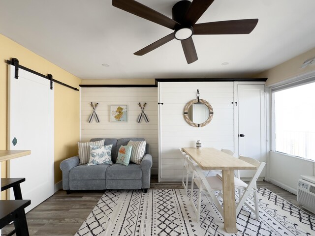 living room featuring a barn door, wood finished floors, ceiling fan, and baseboards