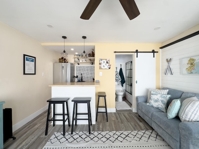 living room with ceiling fan, a barn door, wood finished floors, and baseboards