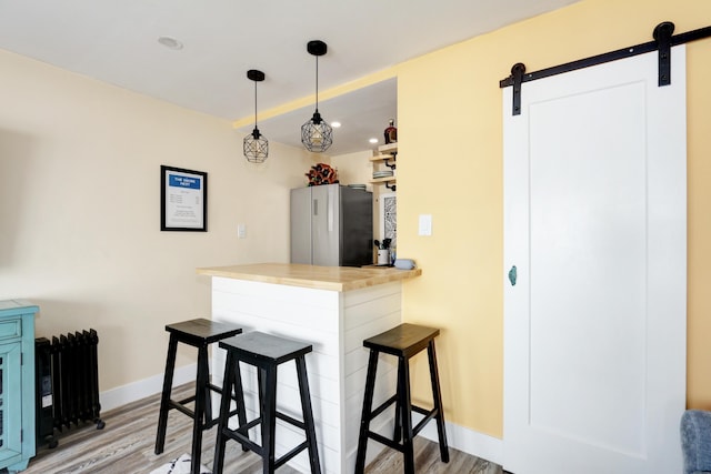 kitchen featuring freestanding refrigerator, light wood-type flooring, a barn door, a kitchen bar, and baseboards