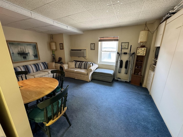 living area with an AC wall unit, carpet flooring, and a drop ceiling