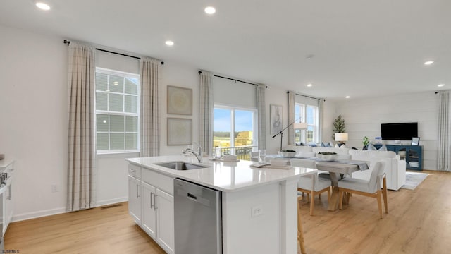 kitchen with a sink, dishwasher, open floor plan, light wood-style flooring, and a kitchen island with sink