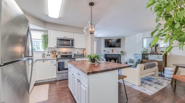 kitchen with appliances with stainless steel finishes, wooden counters, open floor plan, a kitchen breakfast bar, and dark wood-style flooring