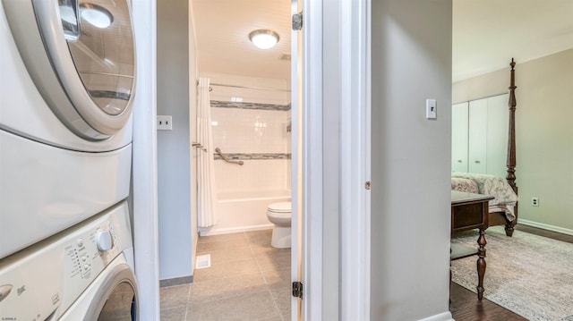 full bath featuring stacked washer / drying machine, baseboards, tile patterned flooring, toilet, and tub / shower combination