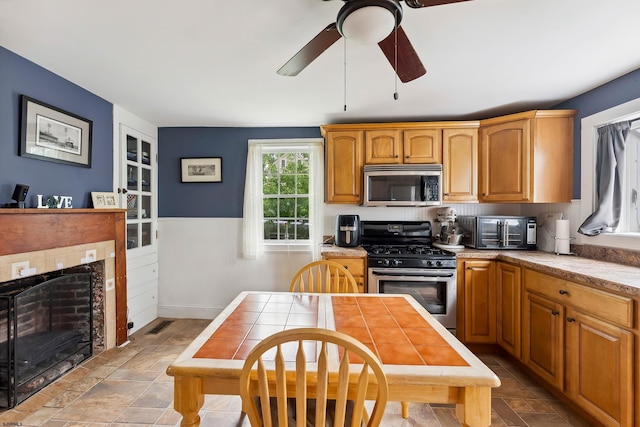 1224 Front St, Mauricetown, NJ 08329 - kitchen with appliances with stainless steel finishes, a ceiling fan, a tiled fireplace, wainscoting, and light countertops