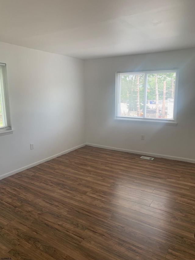 empty room featuring plenty of natural light, dark wood finished floors, and baseboards