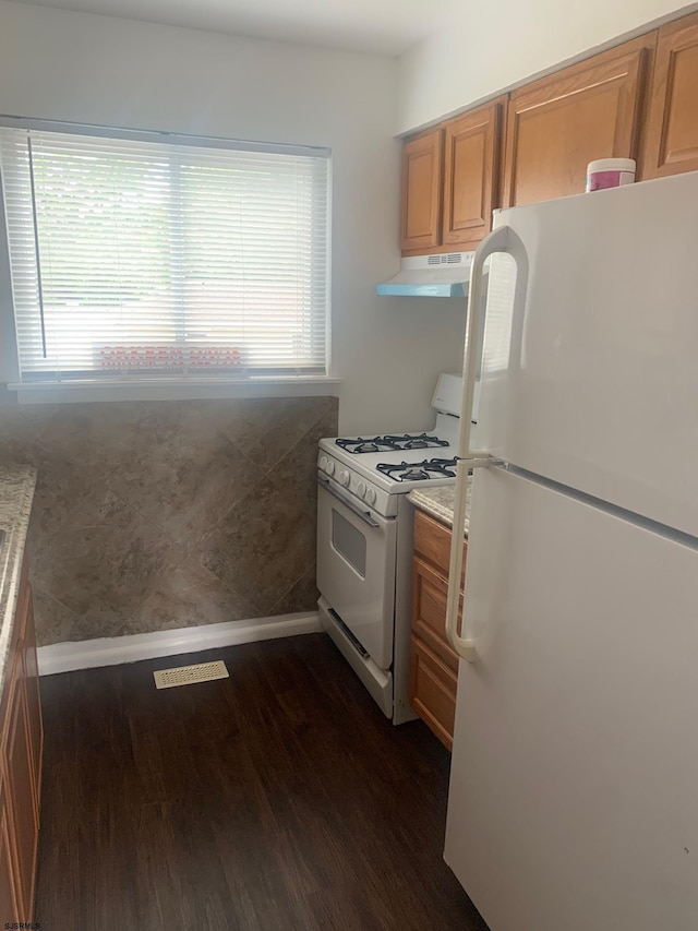 kitchen with white appliances, under cabinet range hood, dark wood-style floors, and brown cabinetry