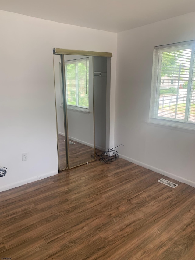 unfurnished bedroom with dark wood-style flooring, baseboards, and a closet