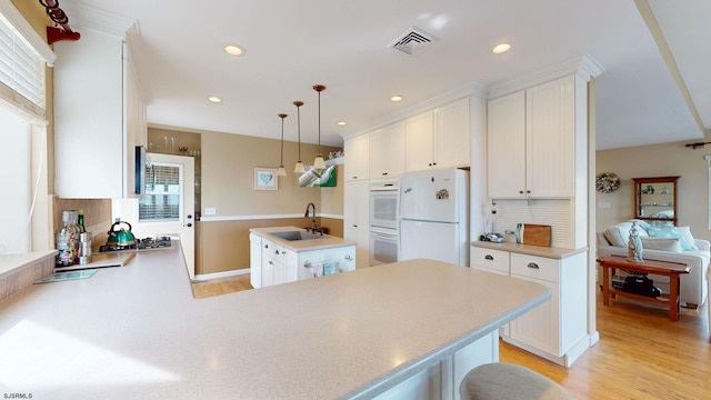 kitchen featuring stainless steel appliances, a center island with sink, a peninsula, light wood-type flooring, and light countertops
