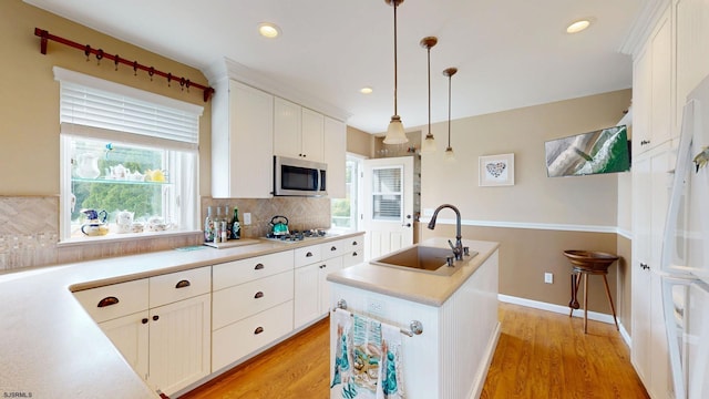 kitchen with a sink, stainless steel microwave, backsplash, a center island with sink, and light wood-type flooring