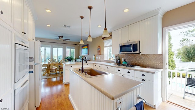 kitchen with white appliances, a sink, ceiling fan, tasteful backsplash, and light wood finished floors