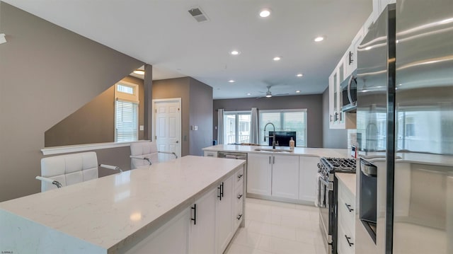 kitchen with appliances with stainless steel finishes, a sink, a peninsula, a kitchen island, and light stone countertops