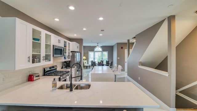 kitchen featuring appliances with stainless steel finishes, a sink, light stone countertops, recessed lighting, and a peninsula