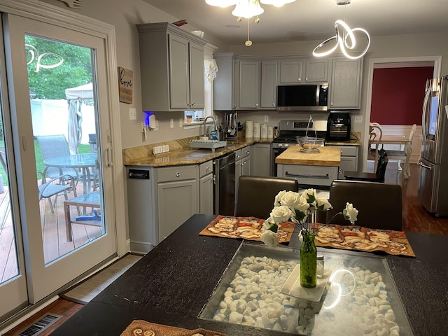 kitchen featuring appliances with stainless steel finishes, gray cabinetry, hanging light fixtures, wood counters, and a sink