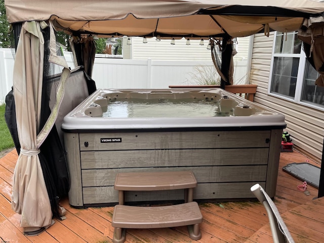 deck with a hot tub, a gazebo, and fence