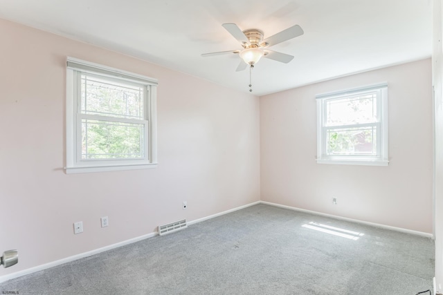 empty room with plenty of natural light, a ceiling fan, carpet, and baseboards