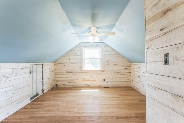 additional living space with wood walls, light wood-style floors, a ceiling fan, and vaulted ceiling
