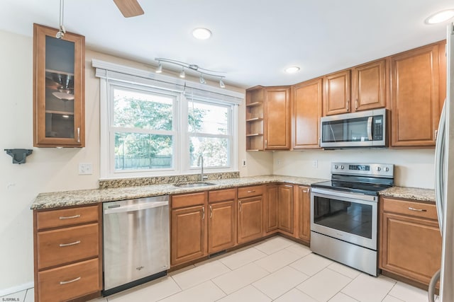 kitchen featuring stainless steel appliances, a sink, brown cabinetry, light stone countertops, and recessed lighting