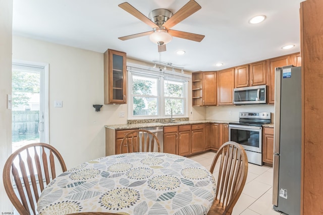 kitchen featuring stainless steel appliances, light tile patterned floors, a sink, brown cabinetry, and ceiling fan