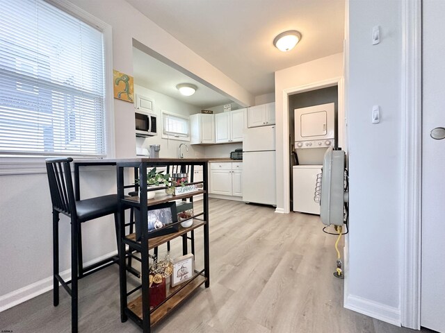 251 38th St, Brigantine, NJ 08203 - kitchen with white appliances, stacked washer / drying machine, white cabinets, baseboards, and light wood-type flooring