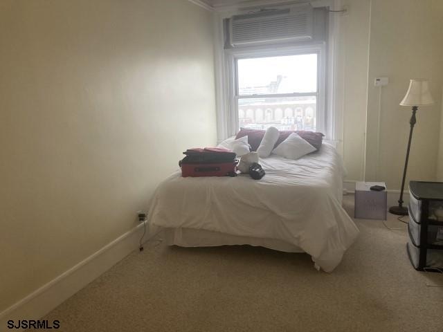 2721 Boardwalk Unit 711, Atlantic City, NJ 08401 - bedroom featuring baseboards, light carpet, an AC wall unit, and ornamental molding