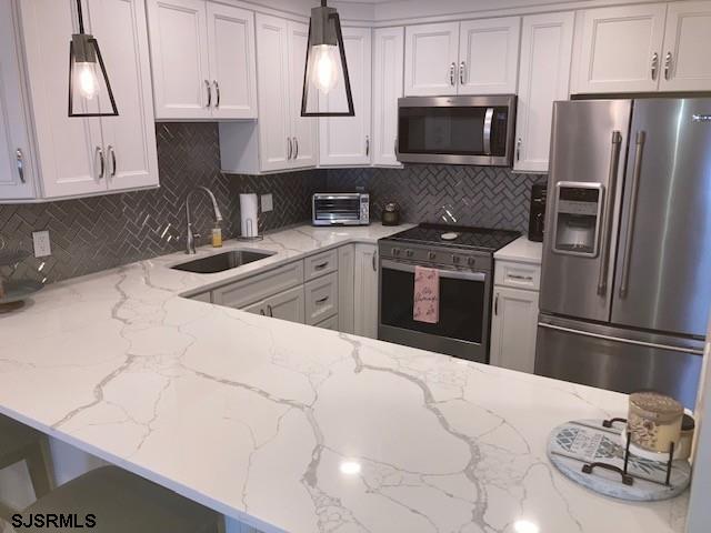 115 35th St Unit 1E, Sea Isle City, NJ 08243 - kitchen featuring stainless steel appliances, a sink, decorative backsplash, and light stone countertops