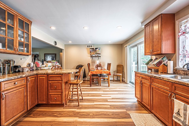 628 1st Ave, Galloway Township, NJ 08205 - kitchen featuring light wood finished floors, a breakfast bar, brown cabinetry, glass insert cabinets, and a peninsula