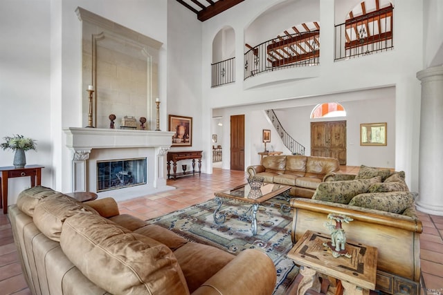 living room featuring tile flooring, a large fireplace, a high ceiling, and decorative columns