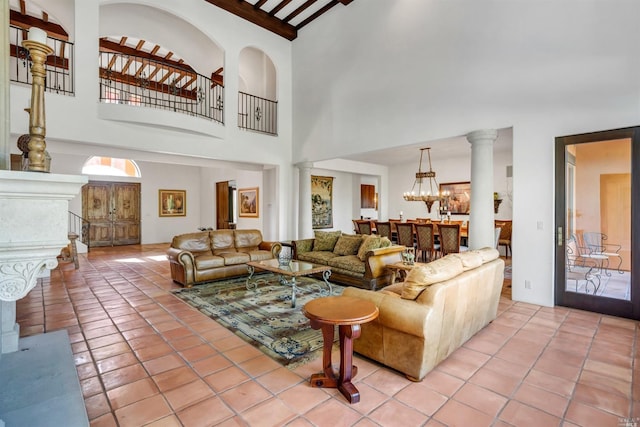 living room with beamed ceiling, a towering ceiling, light tile floors, a notable chandelier, and decorative columns