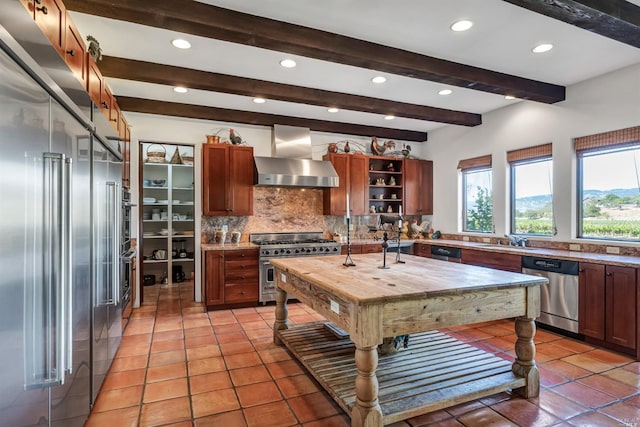 kitchen featuring tasteful backsplash, wall chimney range hood, high end appliances, light tile floors, and butcher block countertops