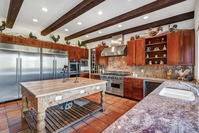 kitchen with backsplash, light tile floors, beam ceiling, wall chimney exhaust hood, and built in appliances