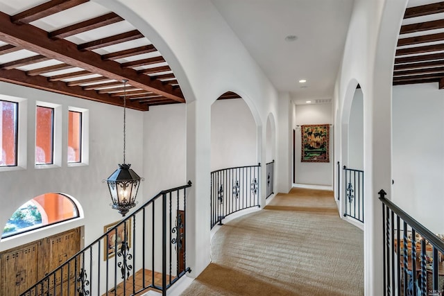 hallway with an inviting chandelier, light colored carpet, and beamed ceiling