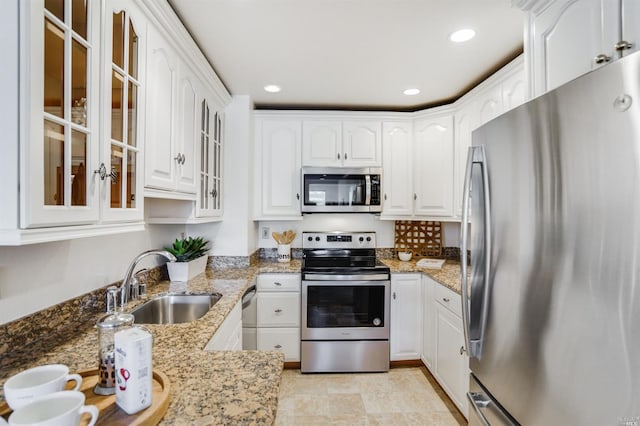 kitchen featuring white cabinets, appliances with stainless steel finishes, light stone counters, and sink