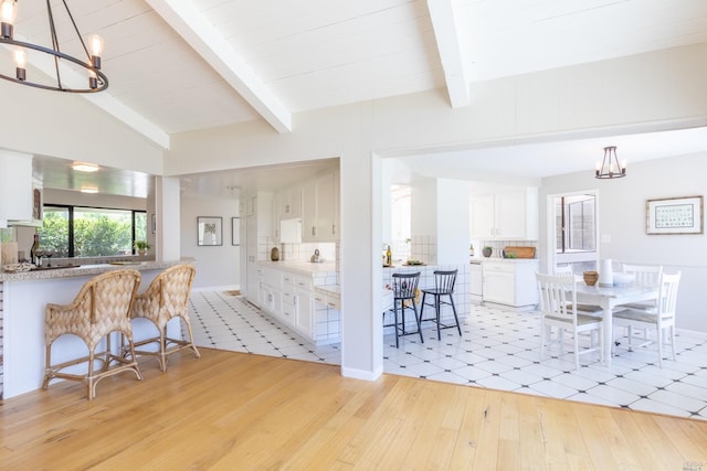 kitchen featuring a notable chandelier, light hardwood / wood-style flooring, white cabinets, lofted ceiling with beams, and tasteful backsplash