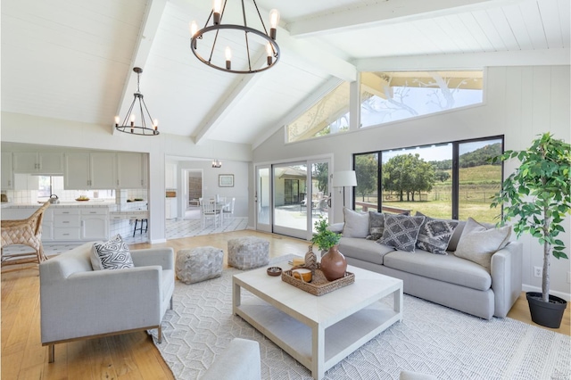 living room with an inviting chandelier, beam ceiling, a wealth of natural light, and light hardwood / wood-style floors