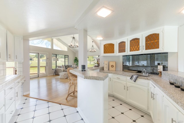 kitchen with an inviting chandelier, lofted ceiling, white cabinetry, and light tile floors