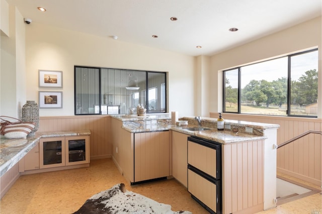 kitchen with kitchen peninsula, light stone counters, and sink