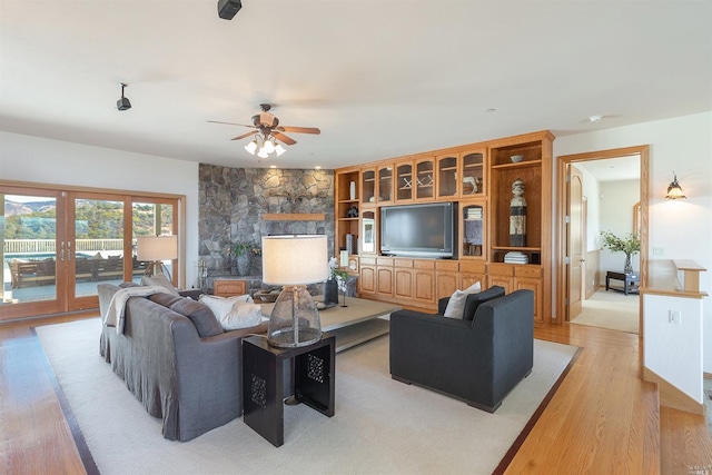 living room with french doors, light hardwood / wood-style floors, ceiling fan, and a stone fireplace