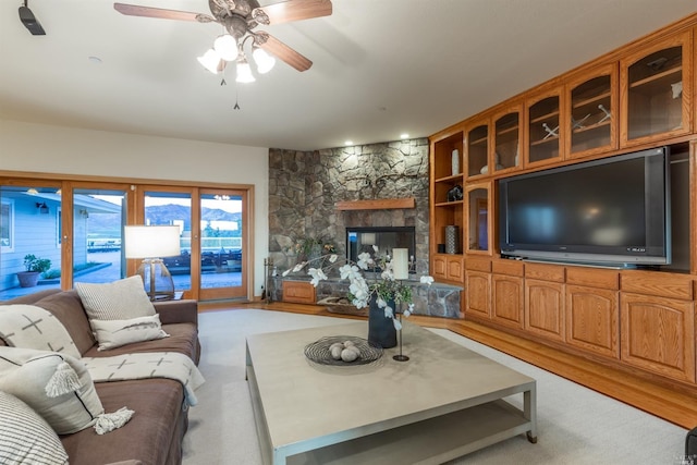 living room featuring light carpet, a stone fireplace, and ceiling fan