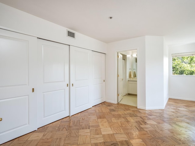 unfurnished bedroom featuring light parquet floors, connected bathroom, and a closet