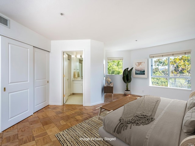 bedroom with light parquet floors, multiple windows, ensuite bathroom, and a closet